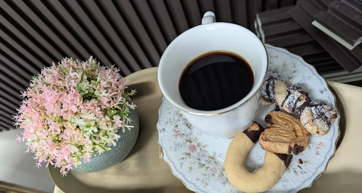 A cup of coffee with cookies on a tray, next to pink flowers