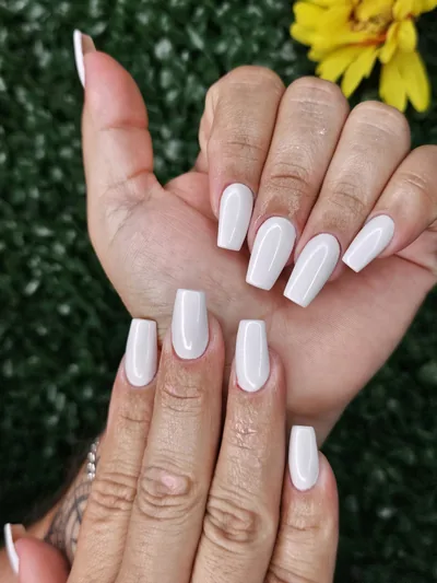 Milky white square nails held up in front of a yellow flower
