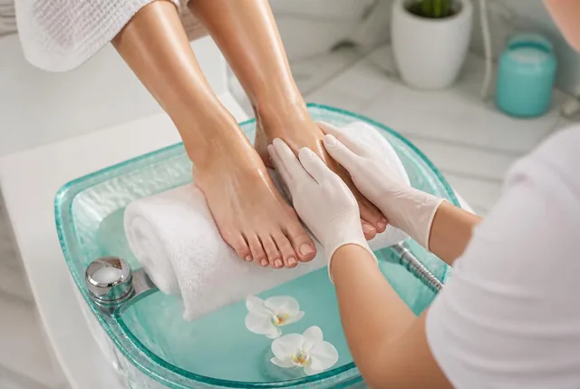 A spa pedicure: feet resting on a white towel over a turquoise foot bath with orchid petals